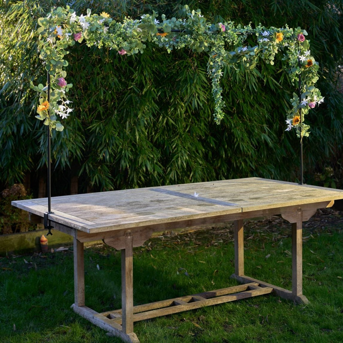Wooden outdoor table with attached floral garland arch.  The arch is decorated with greenery and various flowers.