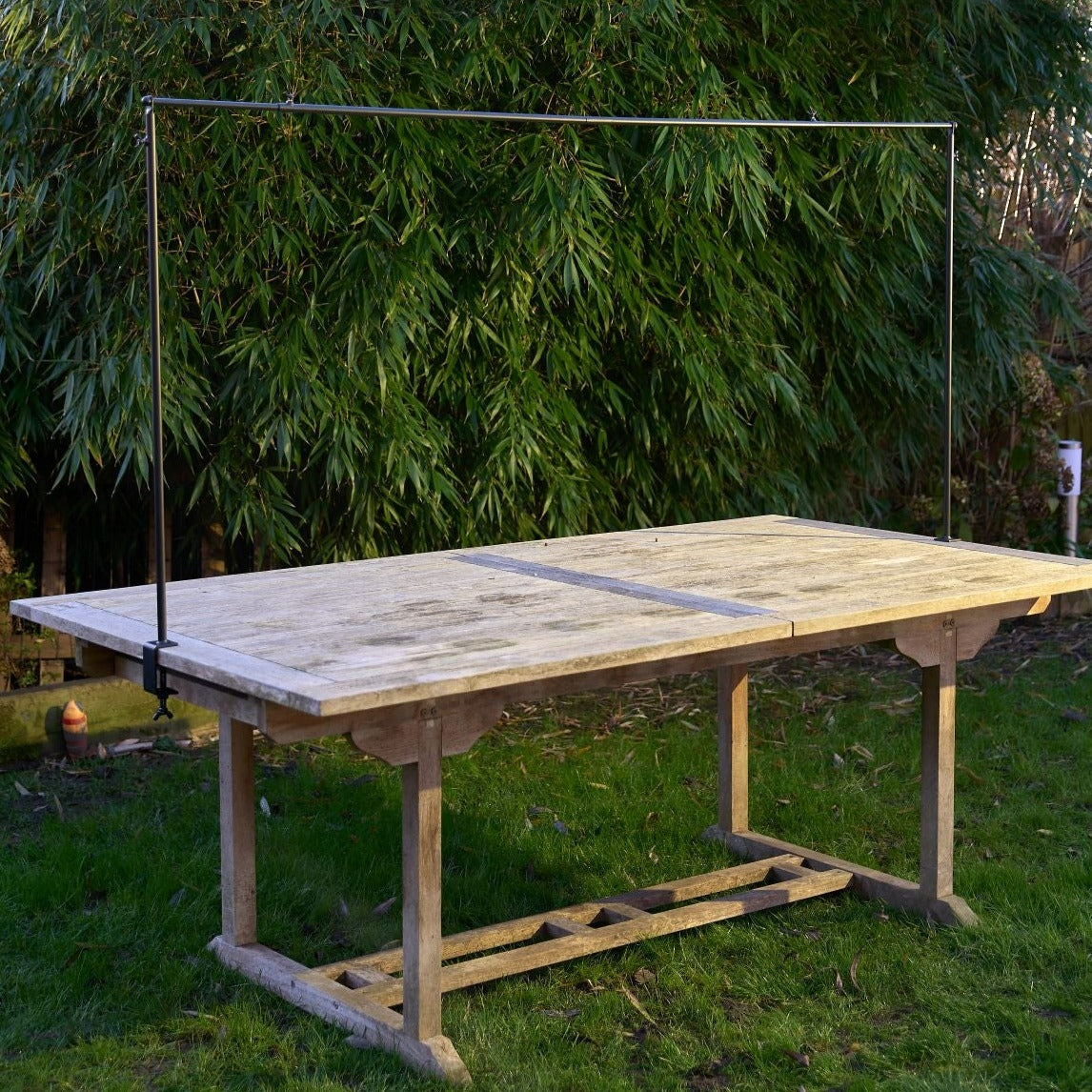 Large, weathered wooden outdoor table with a black metal bar clamped to its surface.