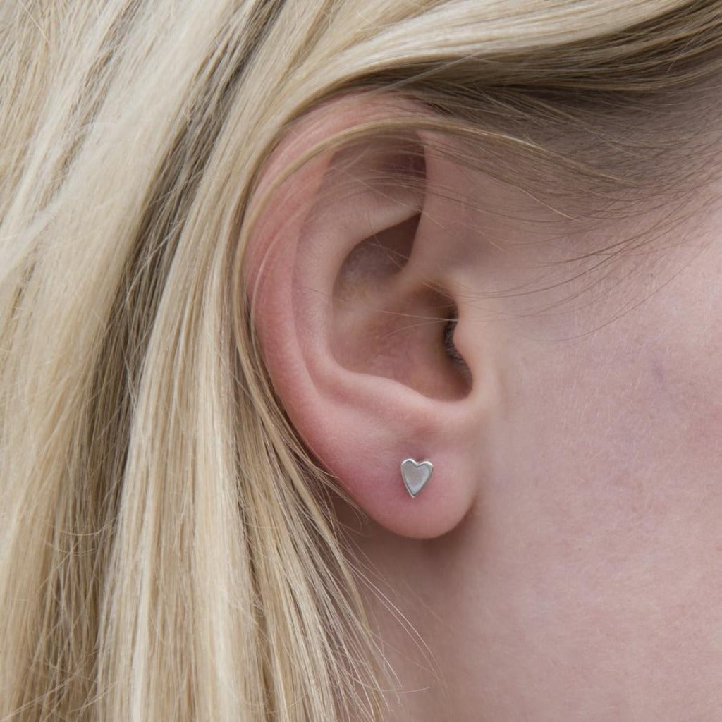 Small silver heart-shaped stud earring in a pierced ear.