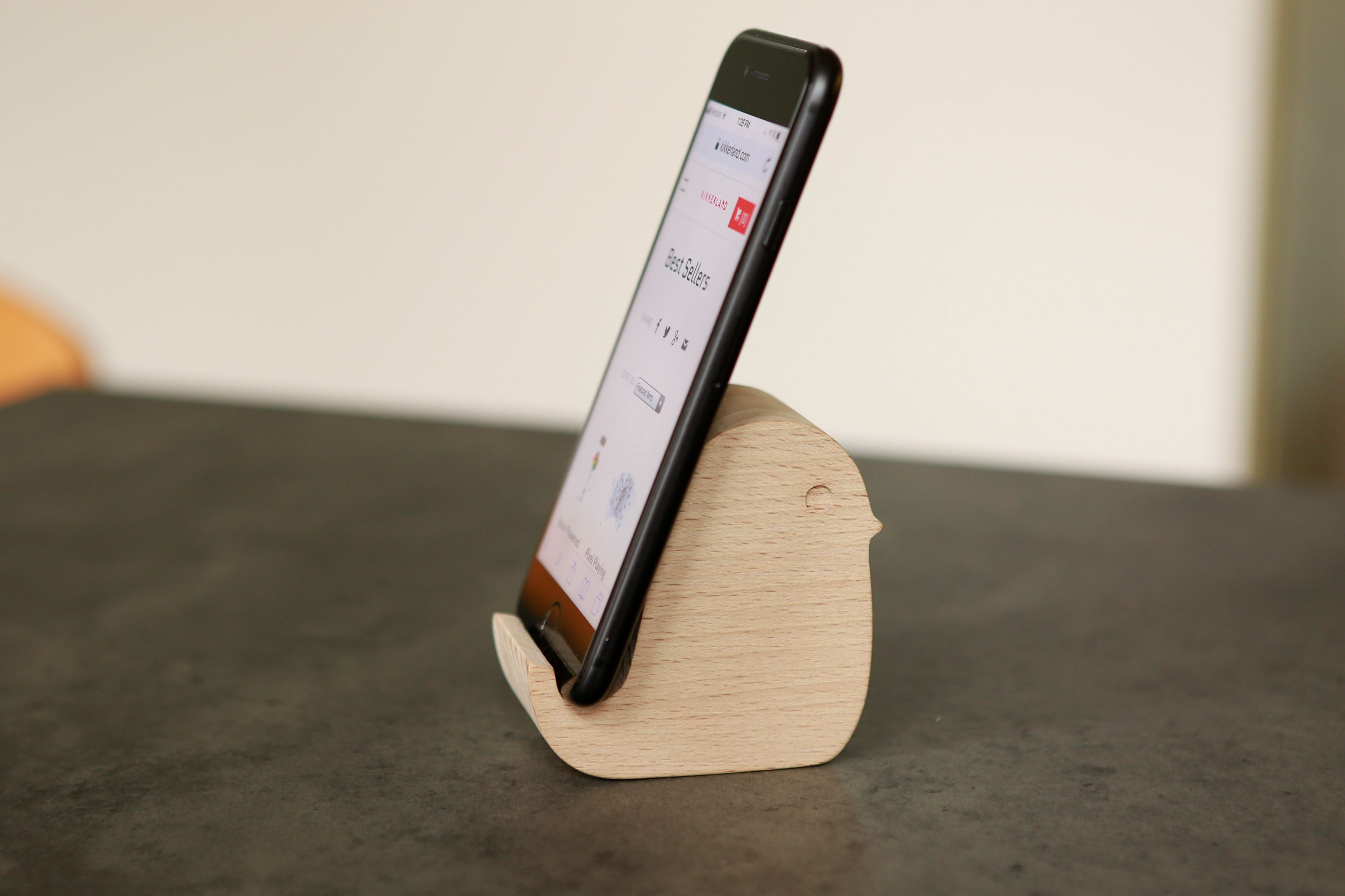 Wooden bird-shaped smartphone stand holding a black smartphone displaying a website.