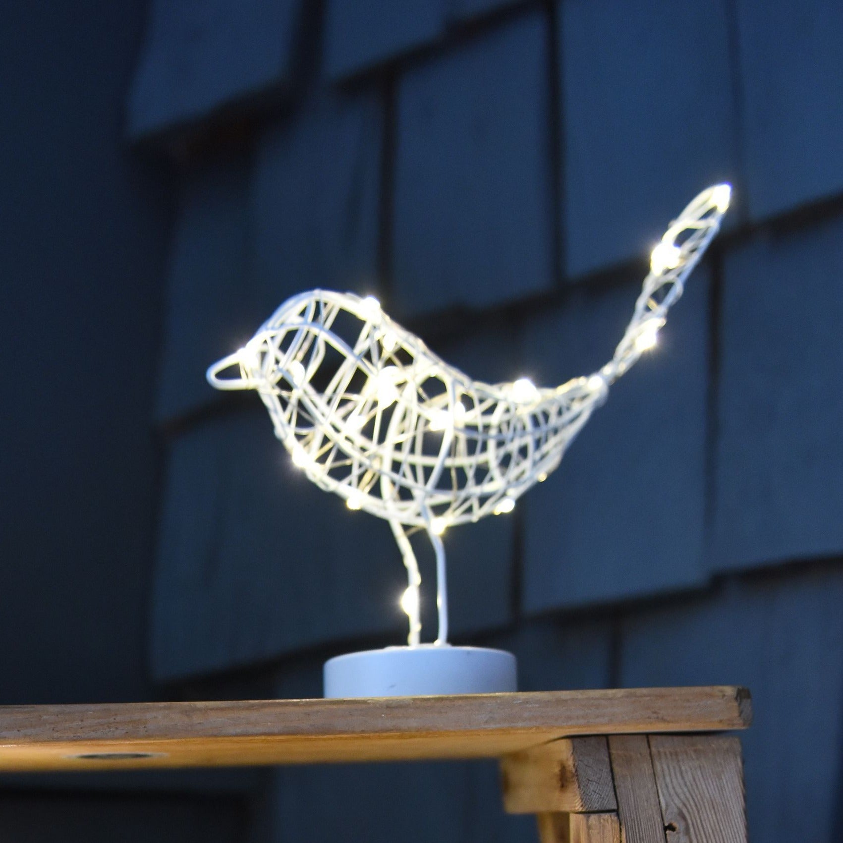 Illuminated wire bird sculpture; white metal frame with embedded LED lights, standing on a small white base.