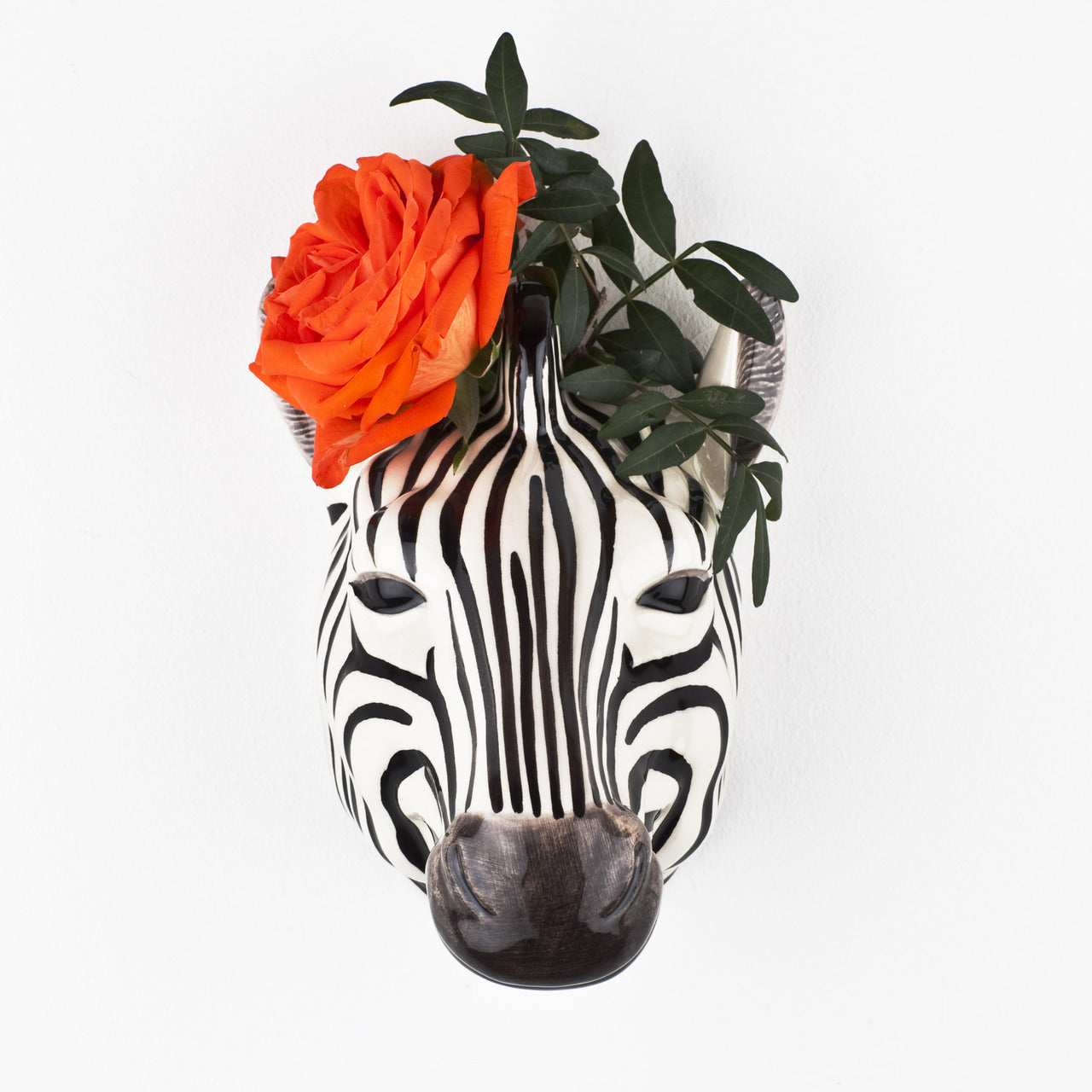 Black and white zebra-shaped planter with an orange rose and green foliage.