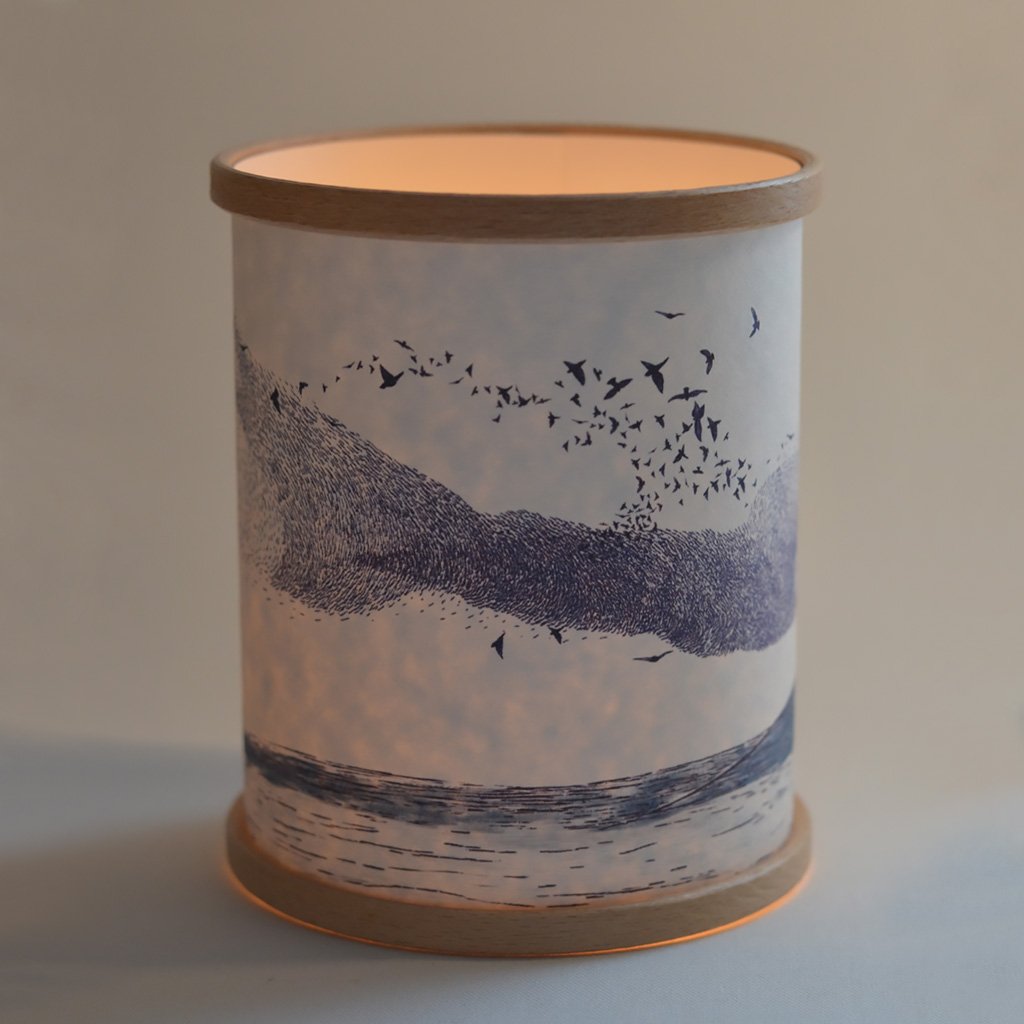 Cylindrical light-up lantern with a wood base and a translucent paper cover featuring a flock of birds flying over a
