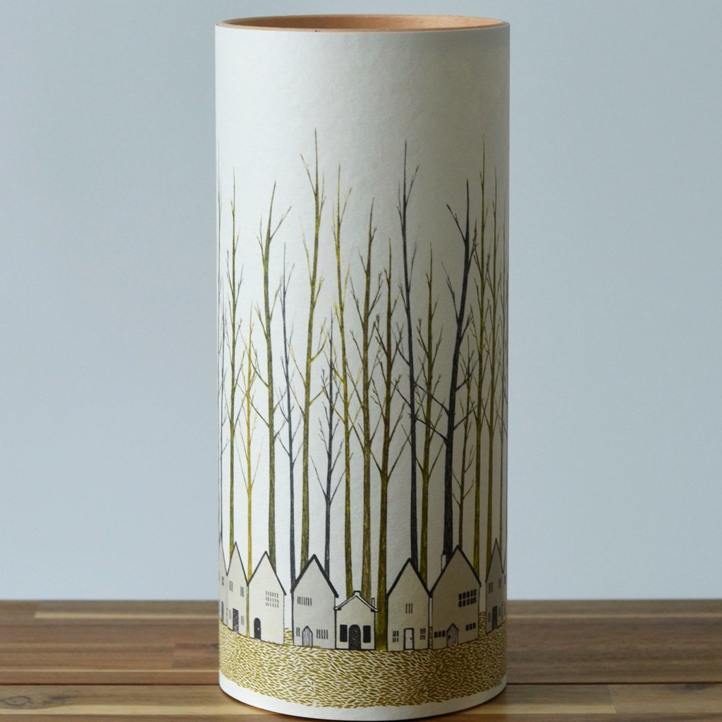 Cylindrical lampshade with a wood top and a cream-colored body featuring a print of stylized trees and houses.