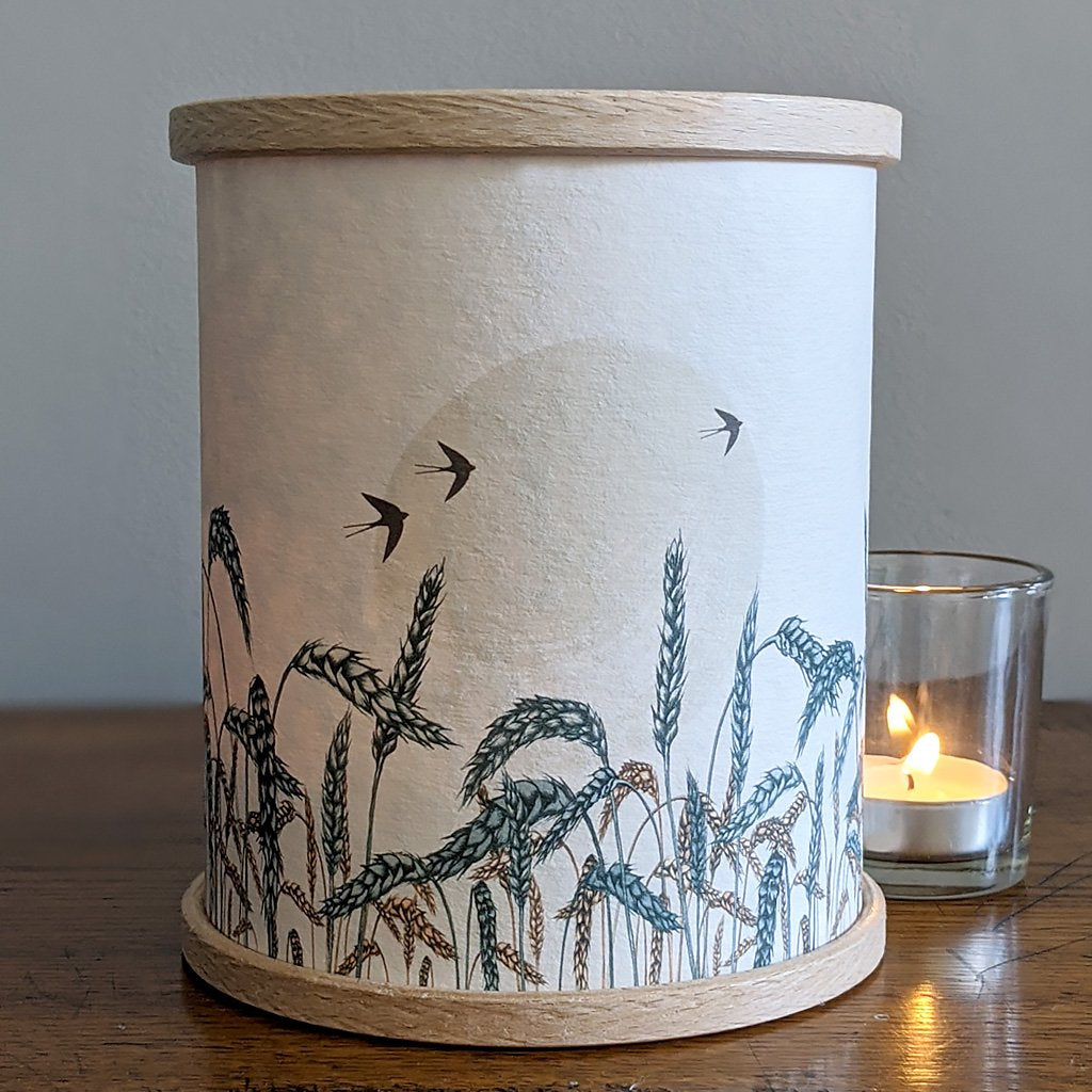 Cylindrical candle lantern with light beige paper cover featuring a wheat field illustration and three birds in flight.