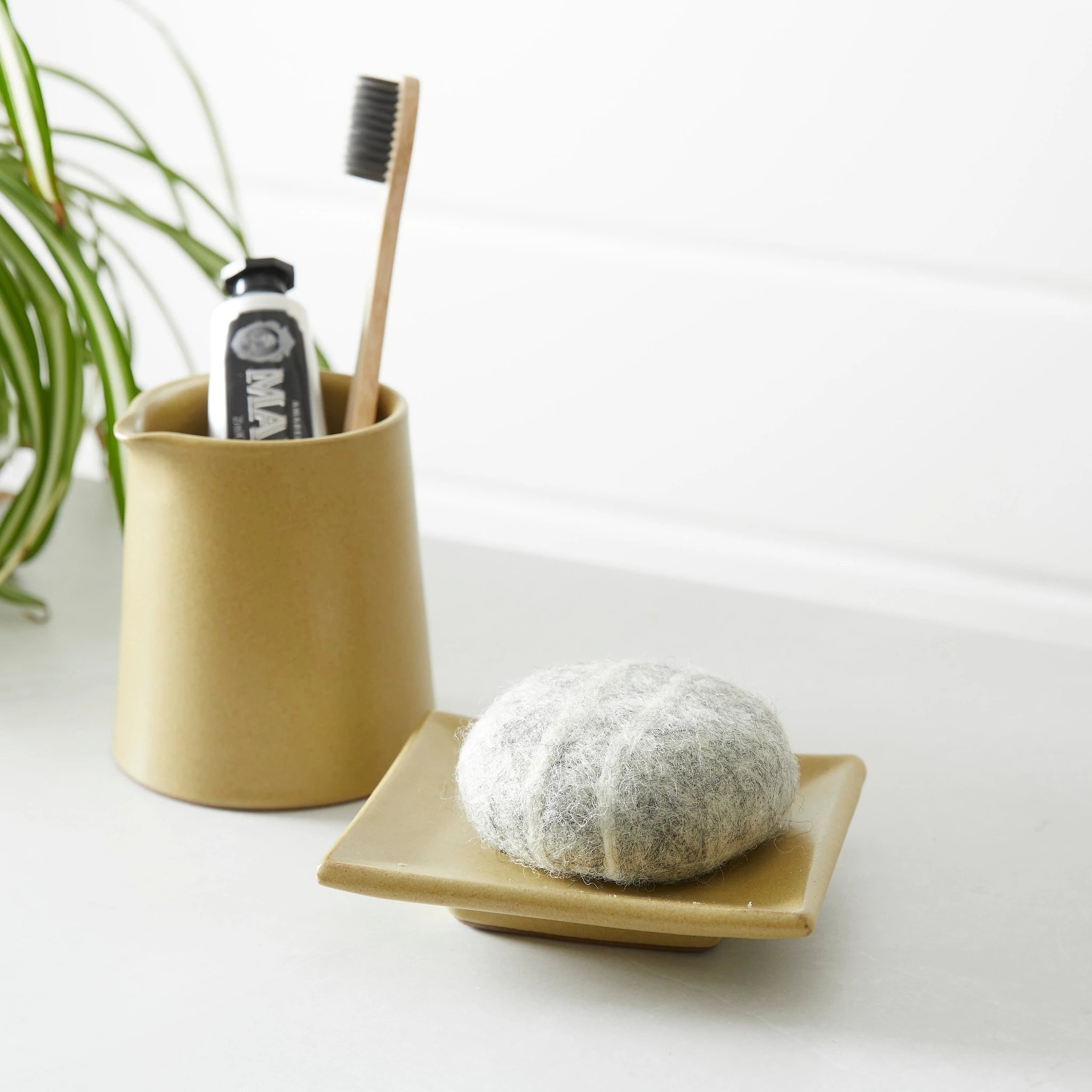 Round gray wool soap on a small, square, tan ceramic dish.