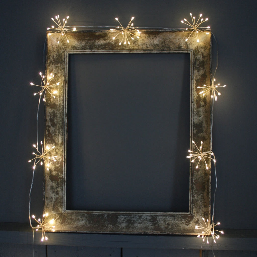 String of warm-white firework lights draped around a rustic wooden picture frame.