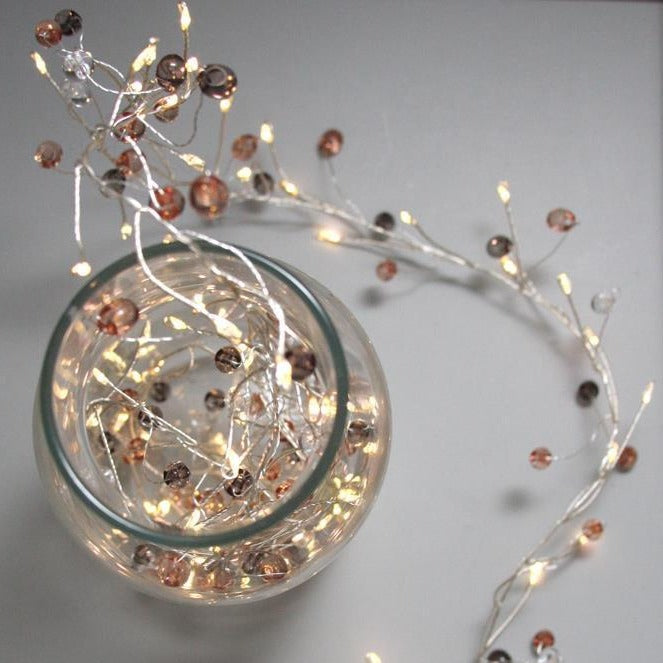 Silver wire string lights with warm white LEDs and small, translucent brown and clear beads.