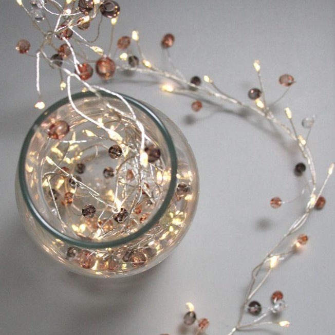 Silver wire string lights with warm white LEDs and rose gold beads.  The lights are partially coiled in a clear glass bowl.