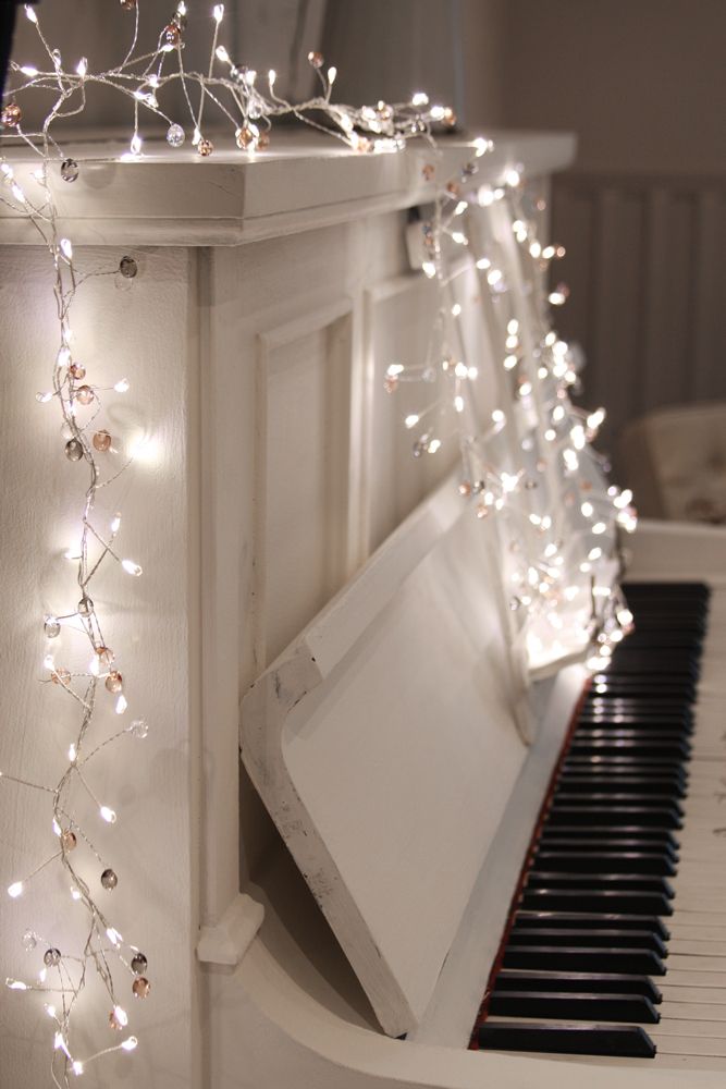 White upright piano adorned with a string of warm-white LED lights and small, clear and rose-gold beads.