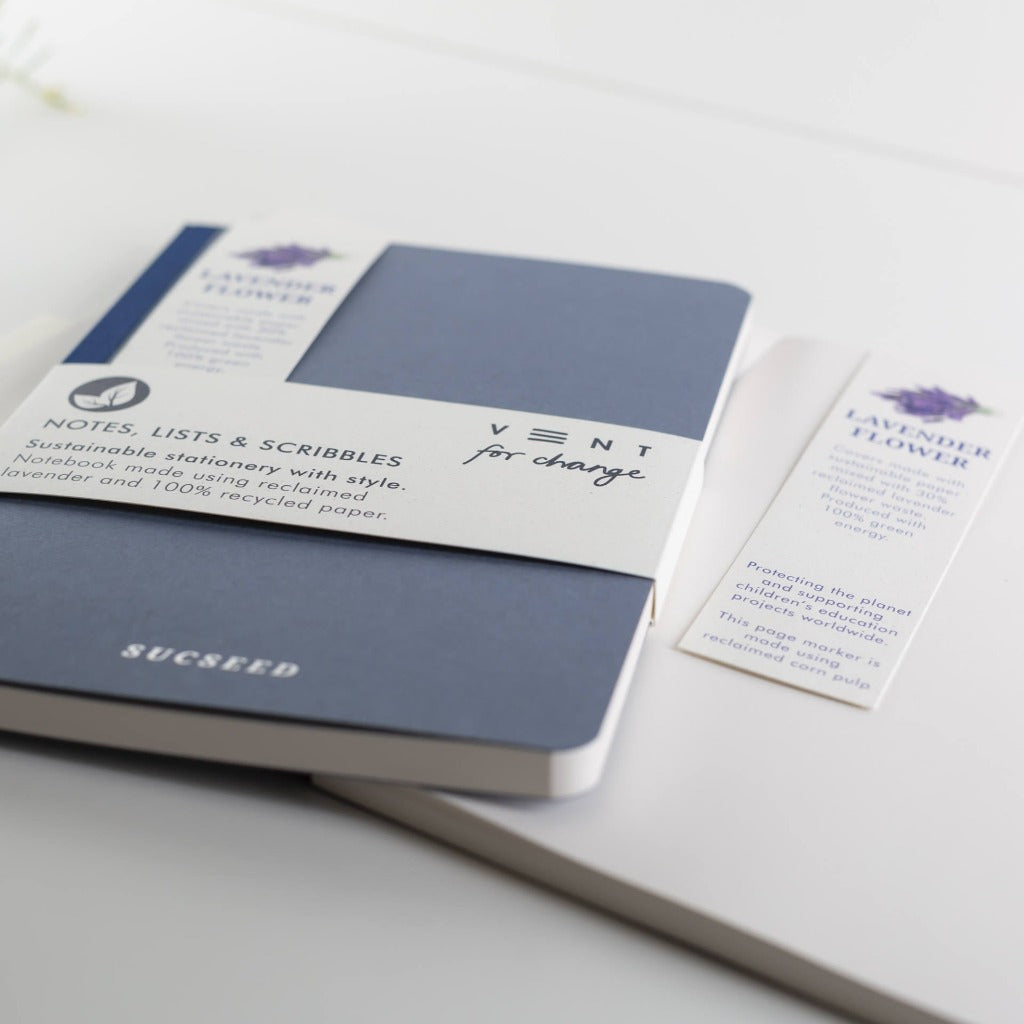 Dark blue notebook made with reclaimed lavender and 100% recycled paper;  "Vent for change" and "Sucseed" branding visible.