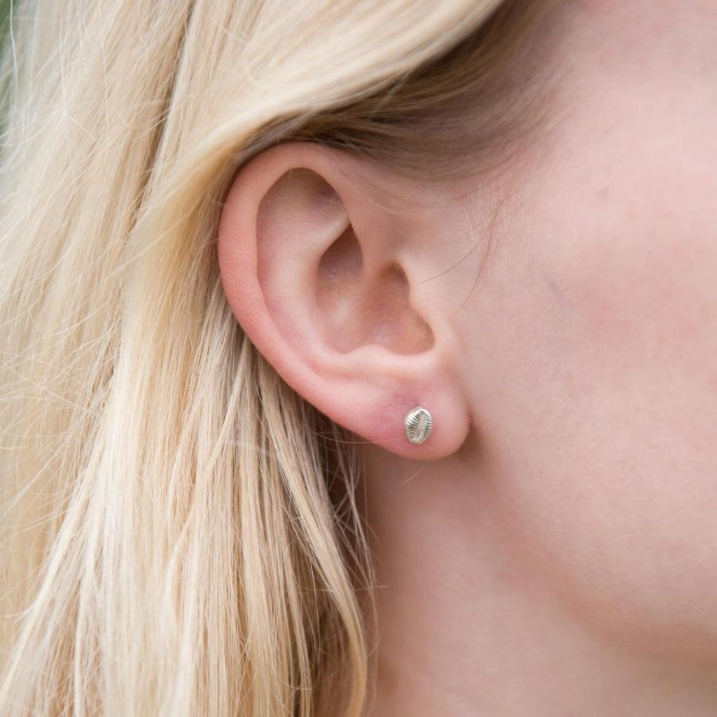 Silver textured stud earring in a person's ear.