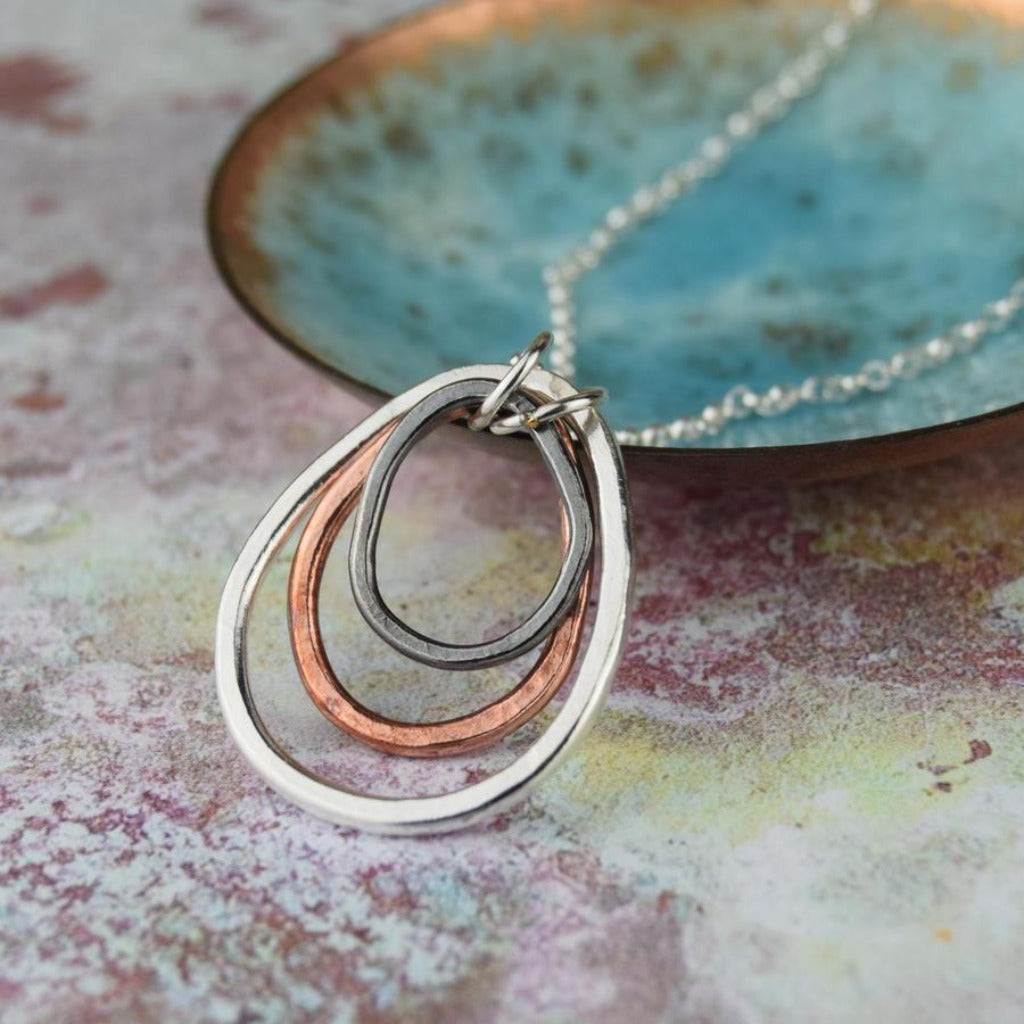 Silver necklace with a pendant featuring three interconnected oval shapes in silver, copper, and dark gray metal.