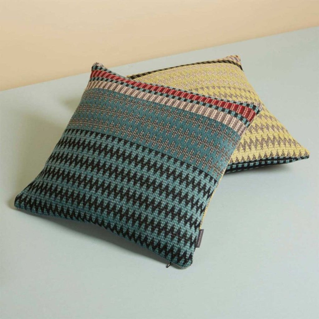 Two textured throw pillows with teal, black, and yellow geometric patterns.  One features a prominent chevron design.