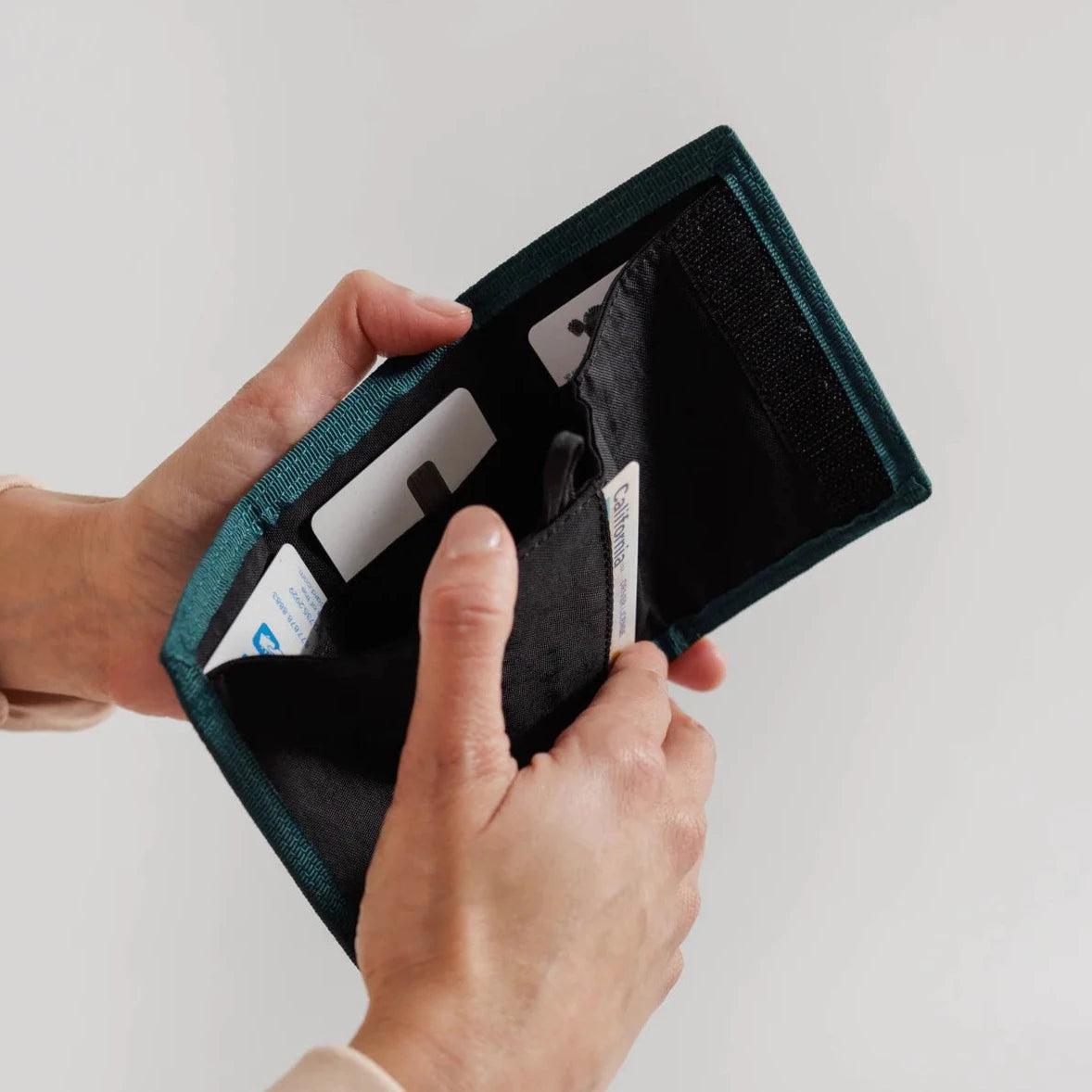 Teal fabric bi-fold wallet open, displaying black interior and several cards.