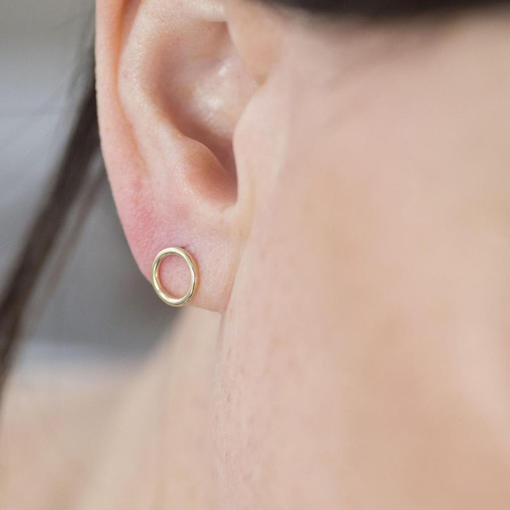 Gold circle stud earring in a person's ear.