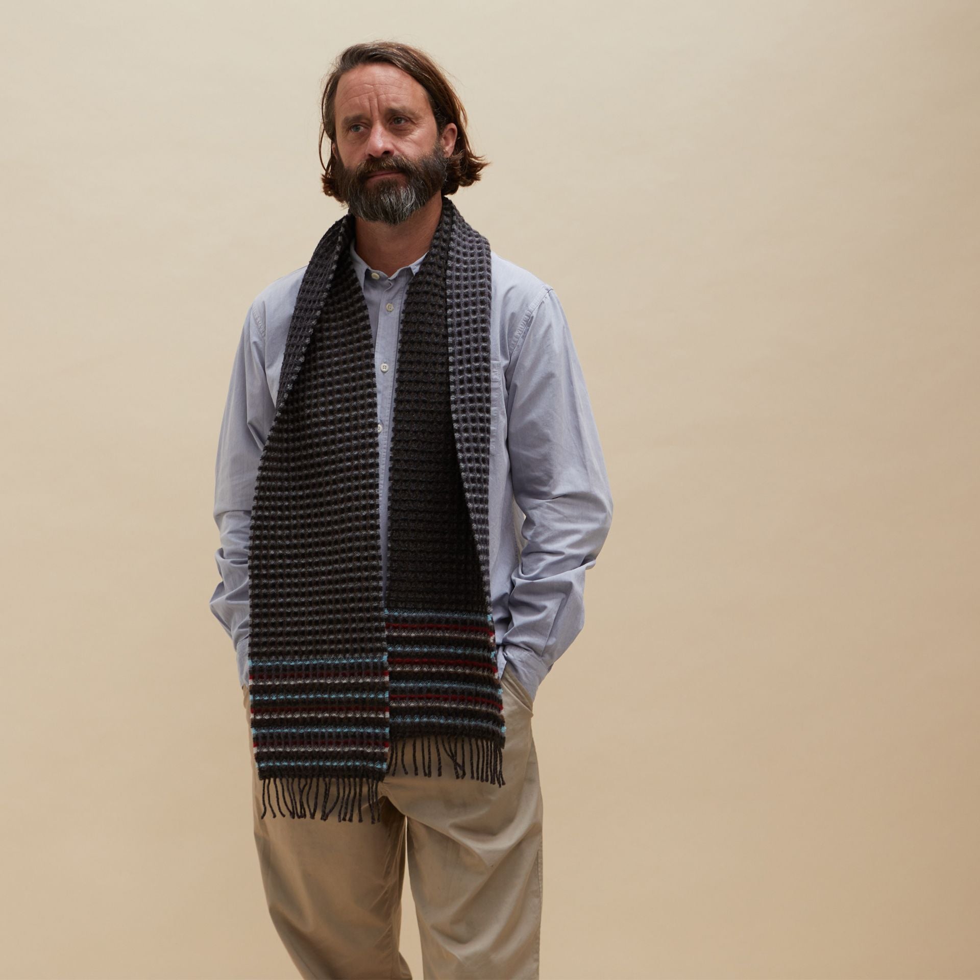 Dark gray waffle-knit wool scarf with multicolored stripes near the bottom and fringed edges.