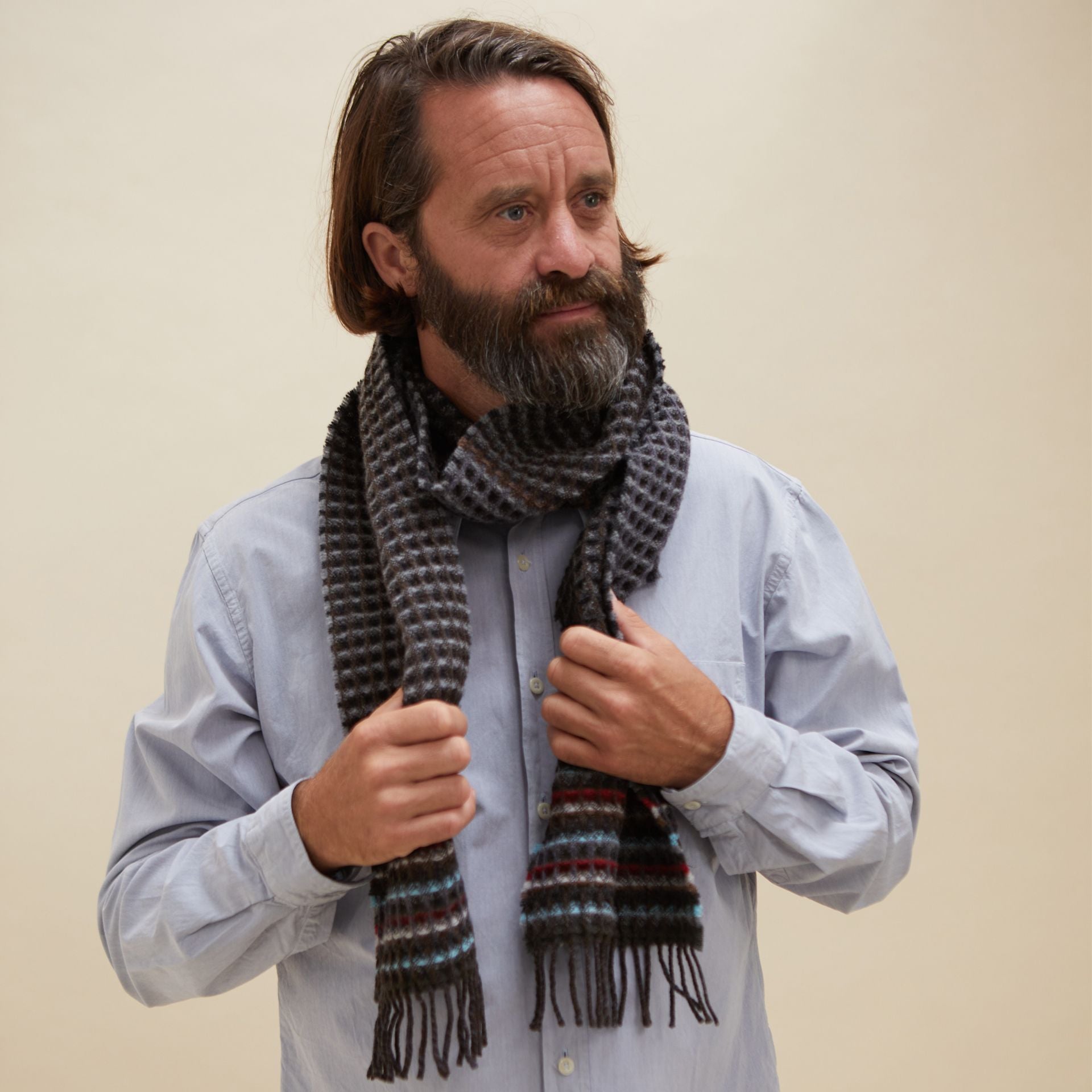 A dark gray waffle-textured scarf with multicolored stripes and fringe, worn by a man.