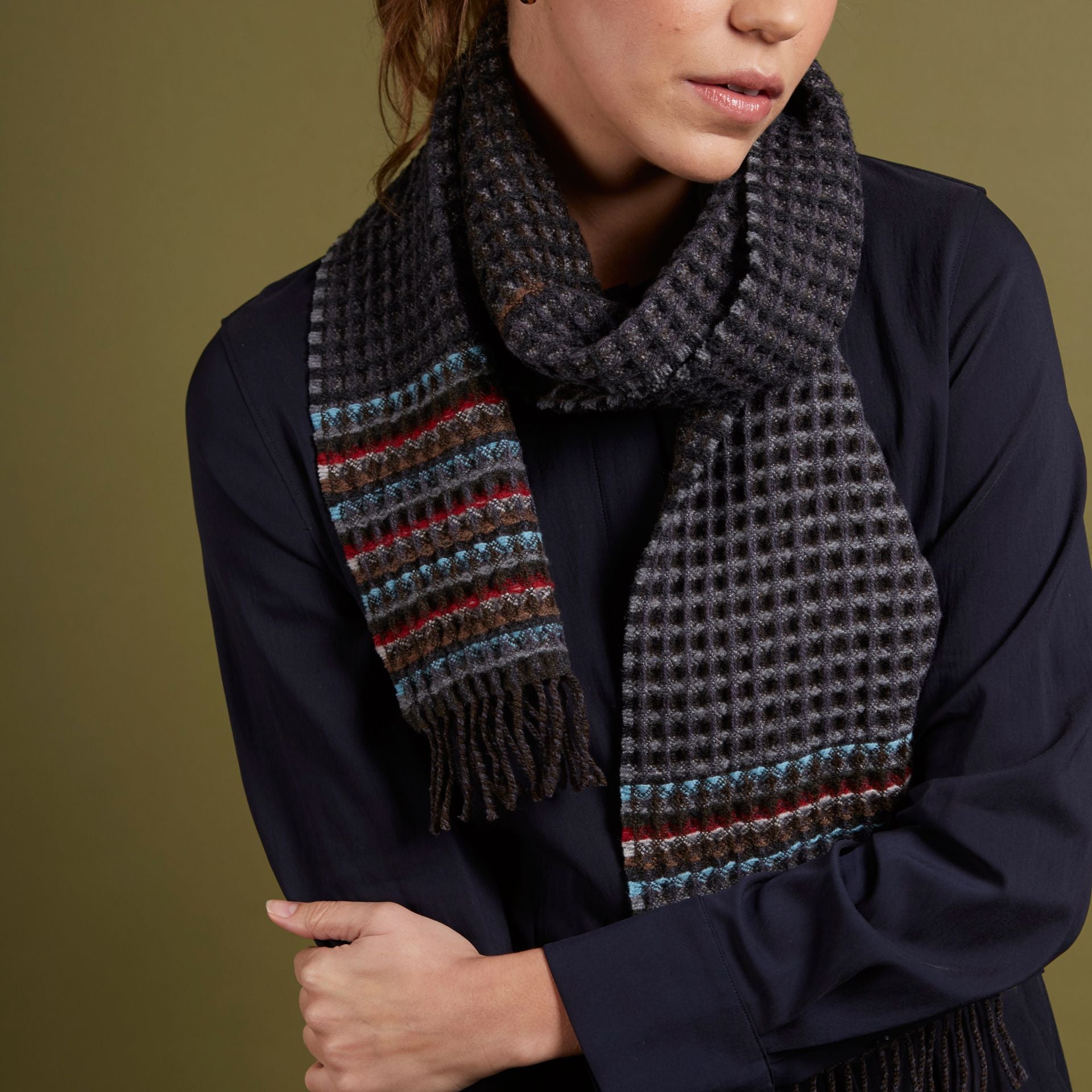 Dark gray waffle-knit wool scarf with multicolored striped detail and fringe.