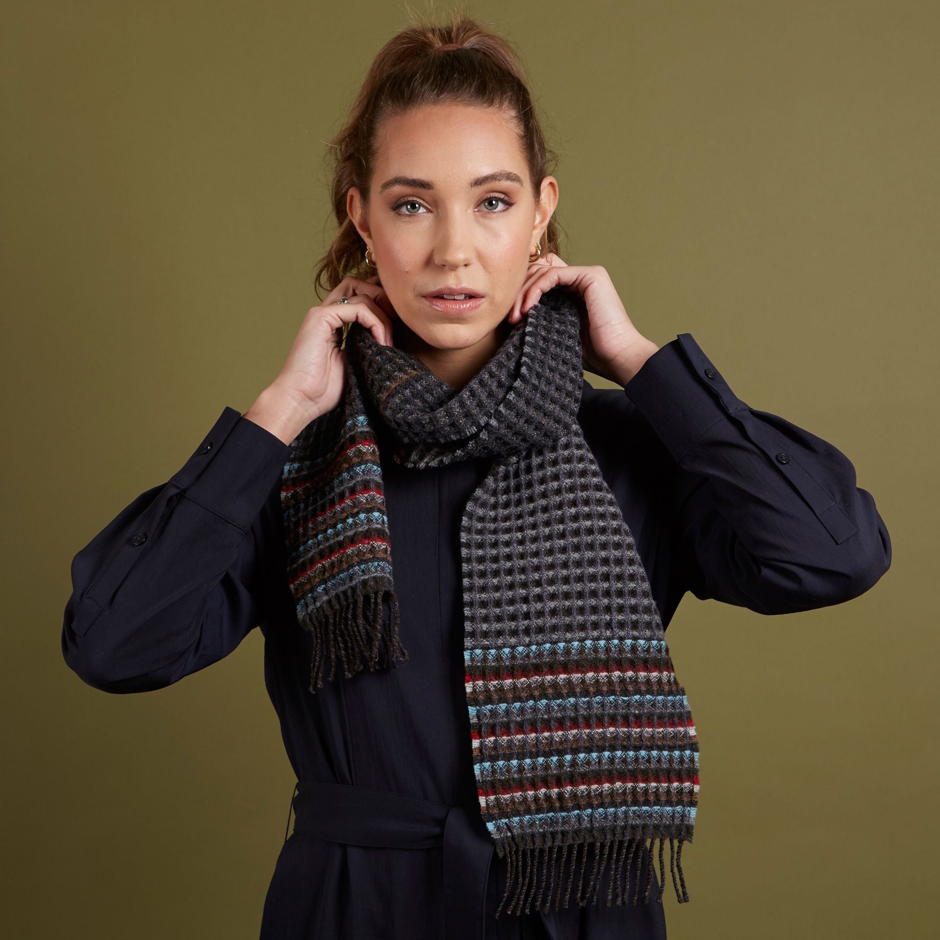 Grey waffle-weave scarf with multicolored striped detail and fringe.