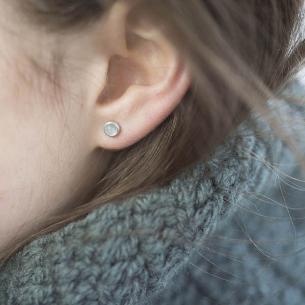 Small, round, light-grey gemstone stud earrings in silver settings.