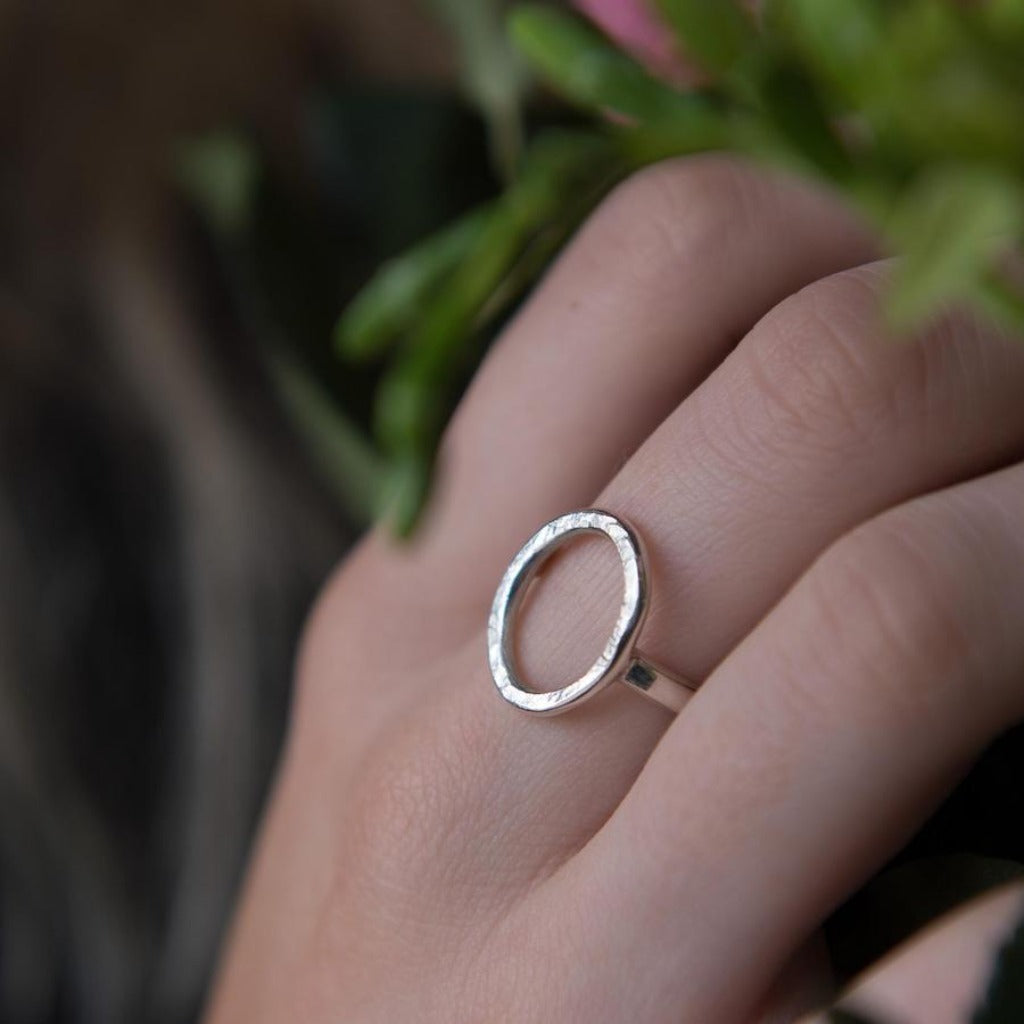 Silver circle ring with a textured band, worn on a finger.