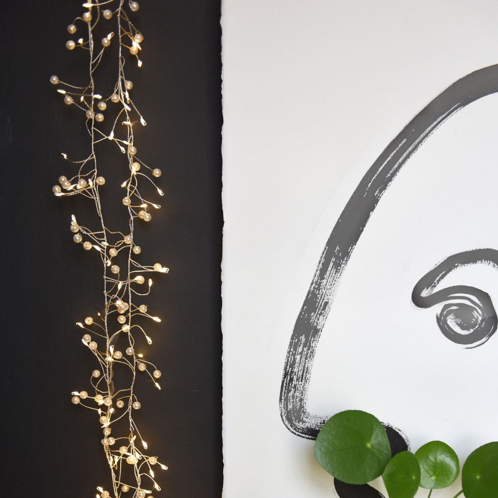 LED fairy lights with pearl-like beads, arranged in a vertical strand against a dark background.