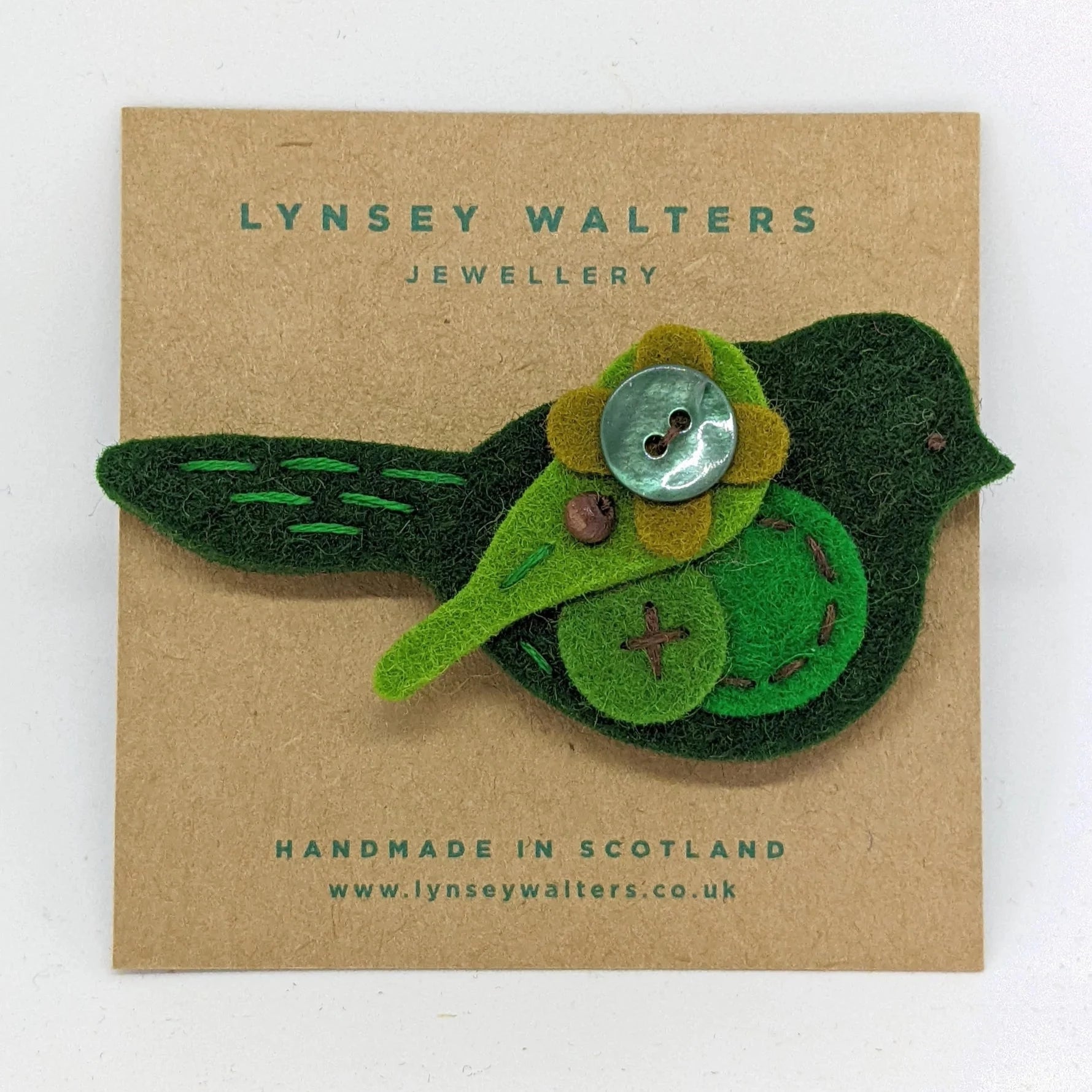 Handmade felt bird brooch in shades of green, featuring a button flower detail and embroidered accents.