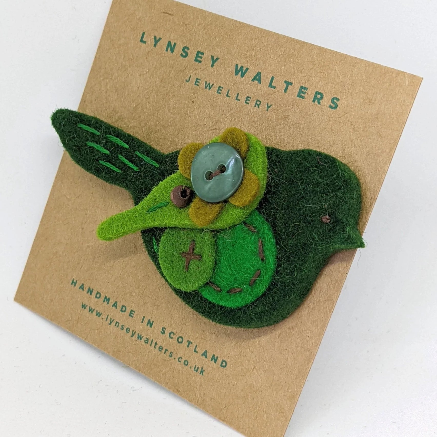 Handmade felt bird brooch in shades of green, featuring a button flower detail.