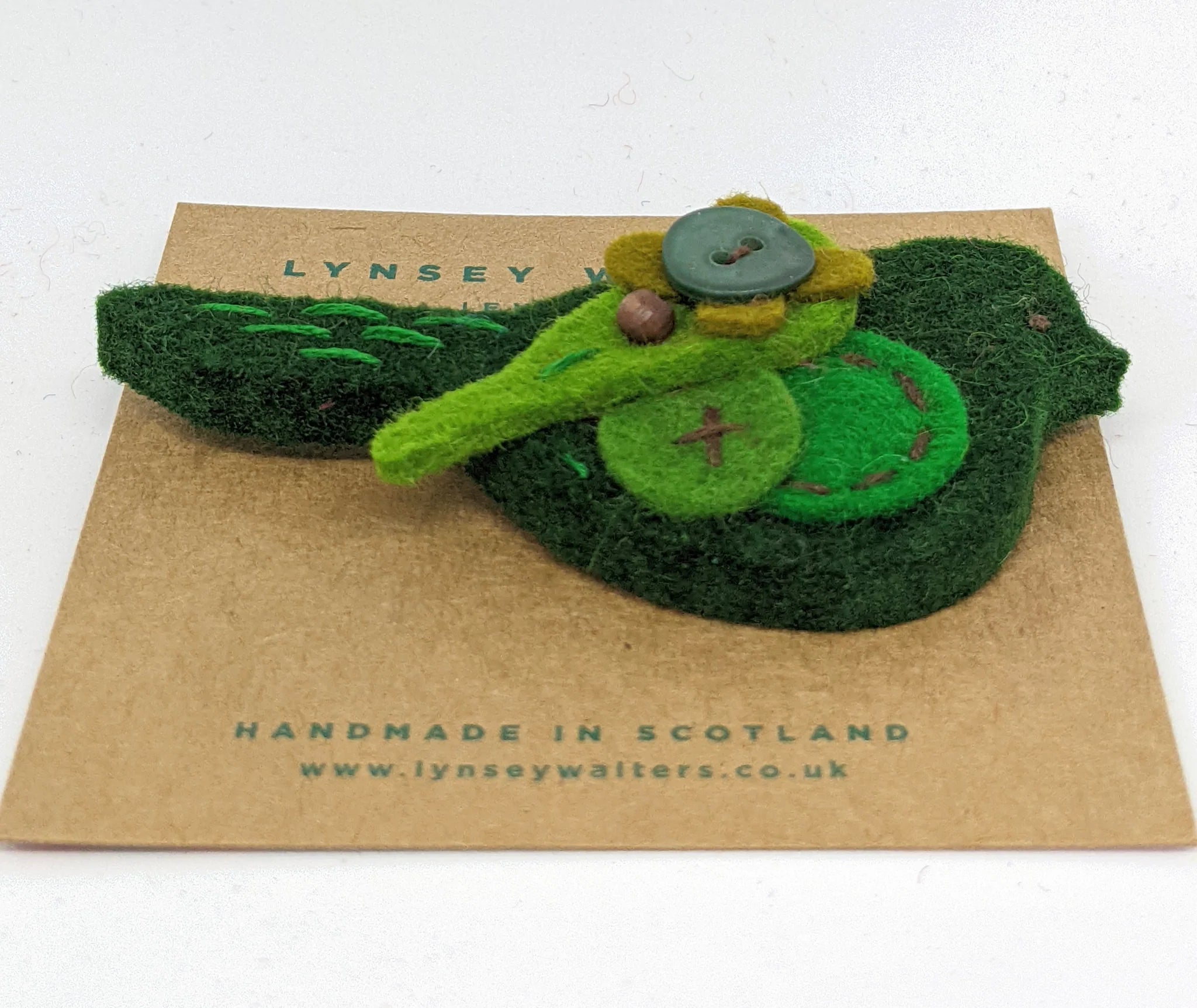 Handmade felt bird brooch in shades of green, featuring embroidered details and button accents.