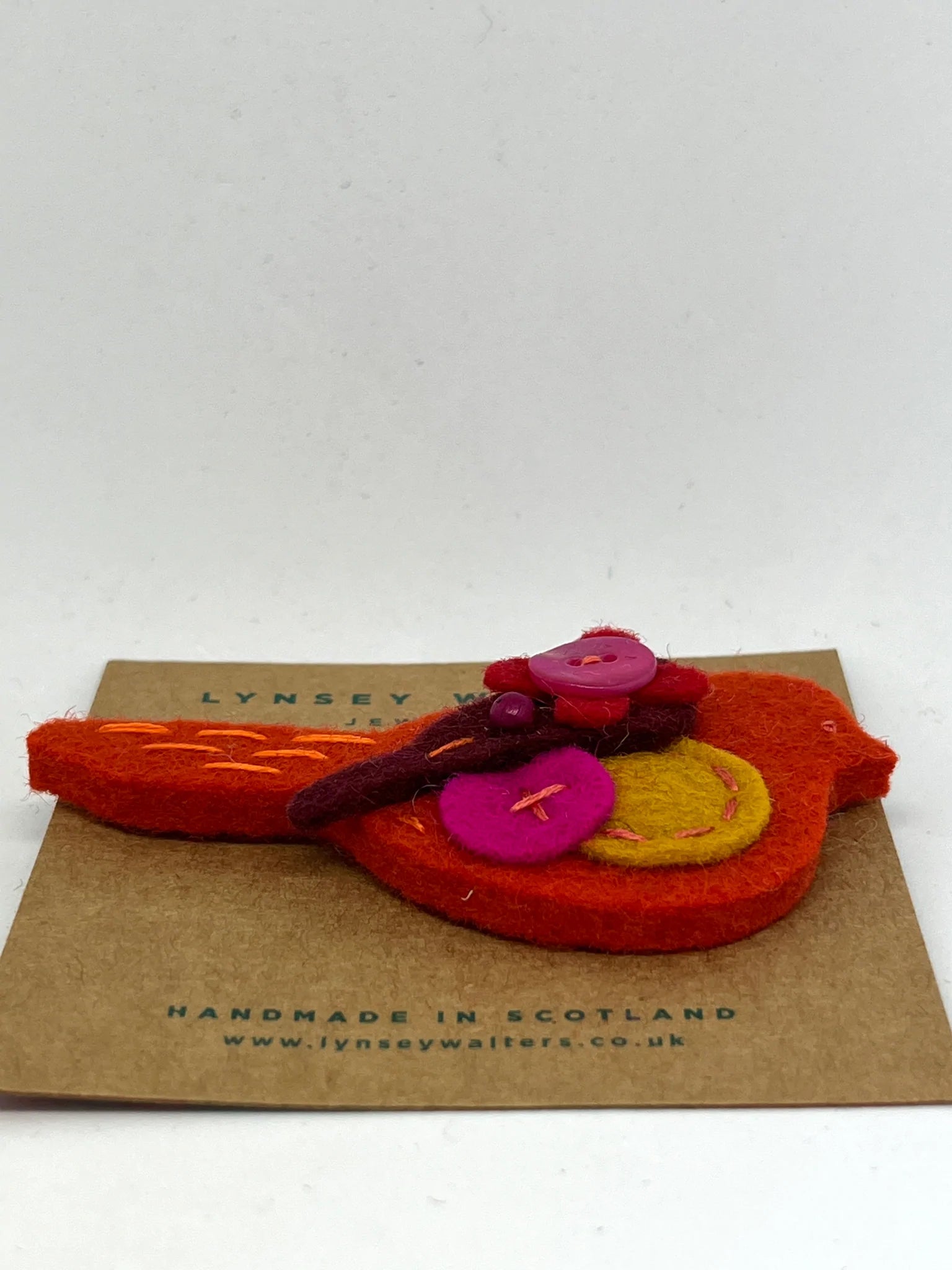 Handmade felt bird brooch in orange, pink, and yellow, adorned with buttons and embroidery.