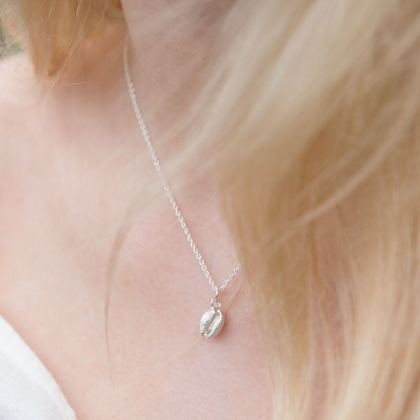 Silver necklace featuring a small, detailed shell pendant on a delicate chain.