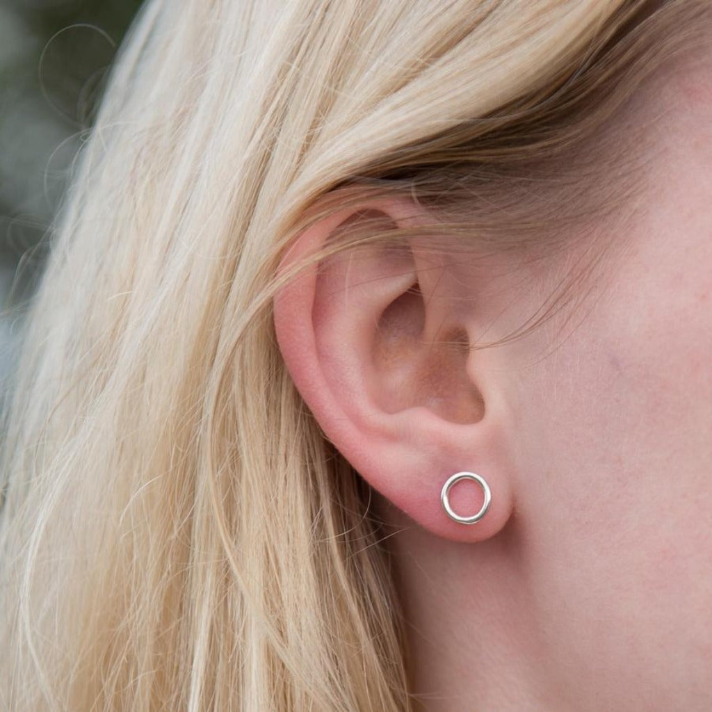 Small silver circle stud earrings in a person's ear.