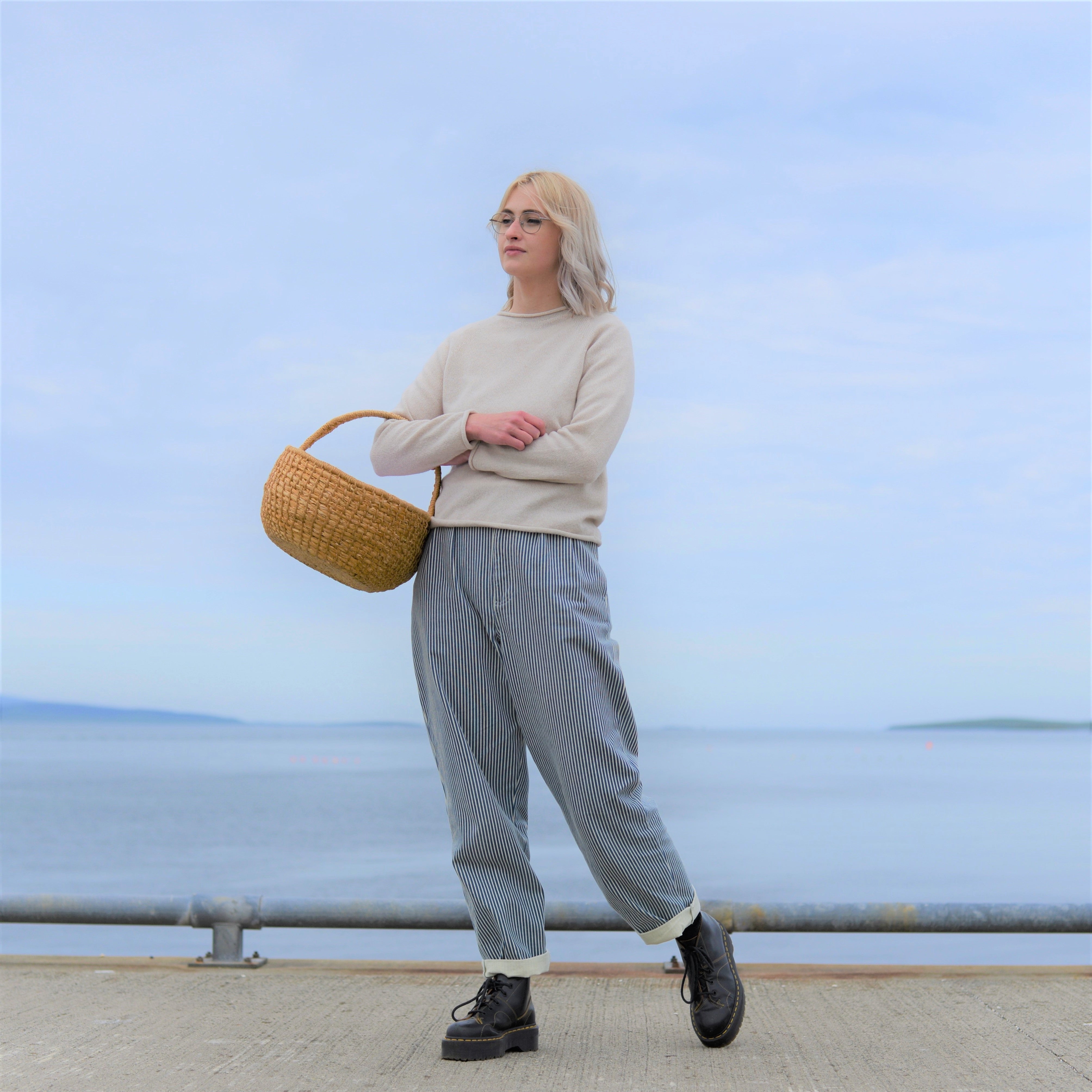 Woman in beige sweater and striped pants carries a woven basket, wearing black platform boots.