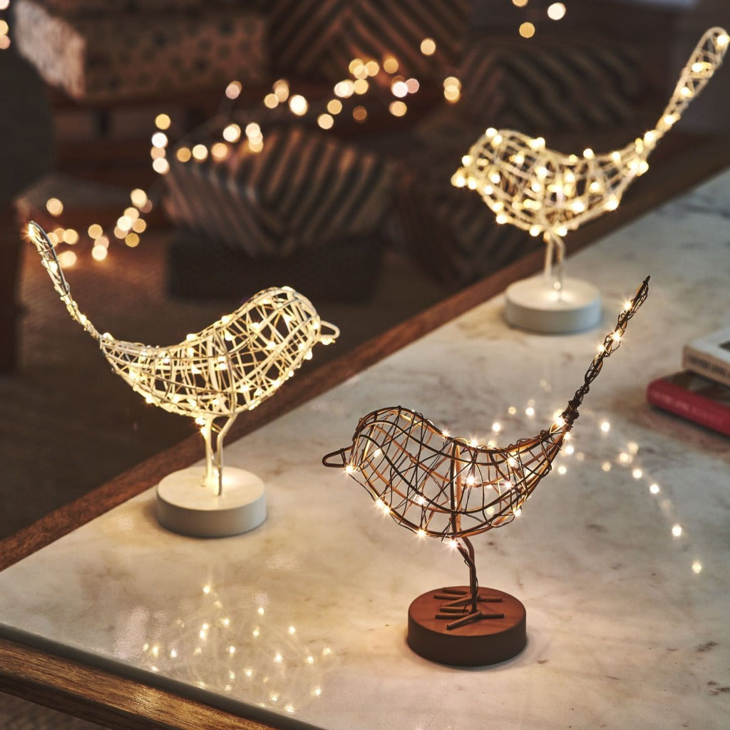 Three wire bird sculptures with embedded LED lights; two are light-colored wire, one is darker.  Each sits on a small base.