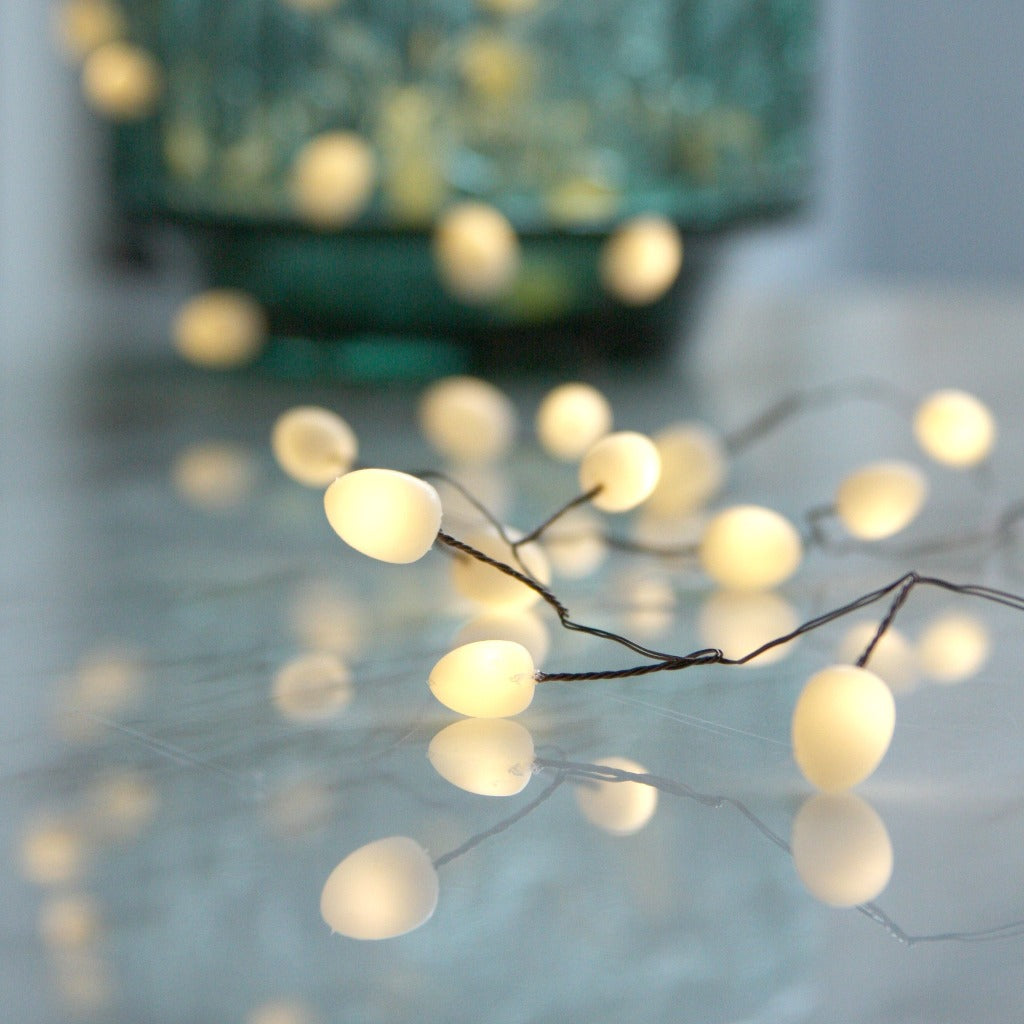 String of warm-white LED lights with oval-shaped bulbs, arranged on a reflective surface.
