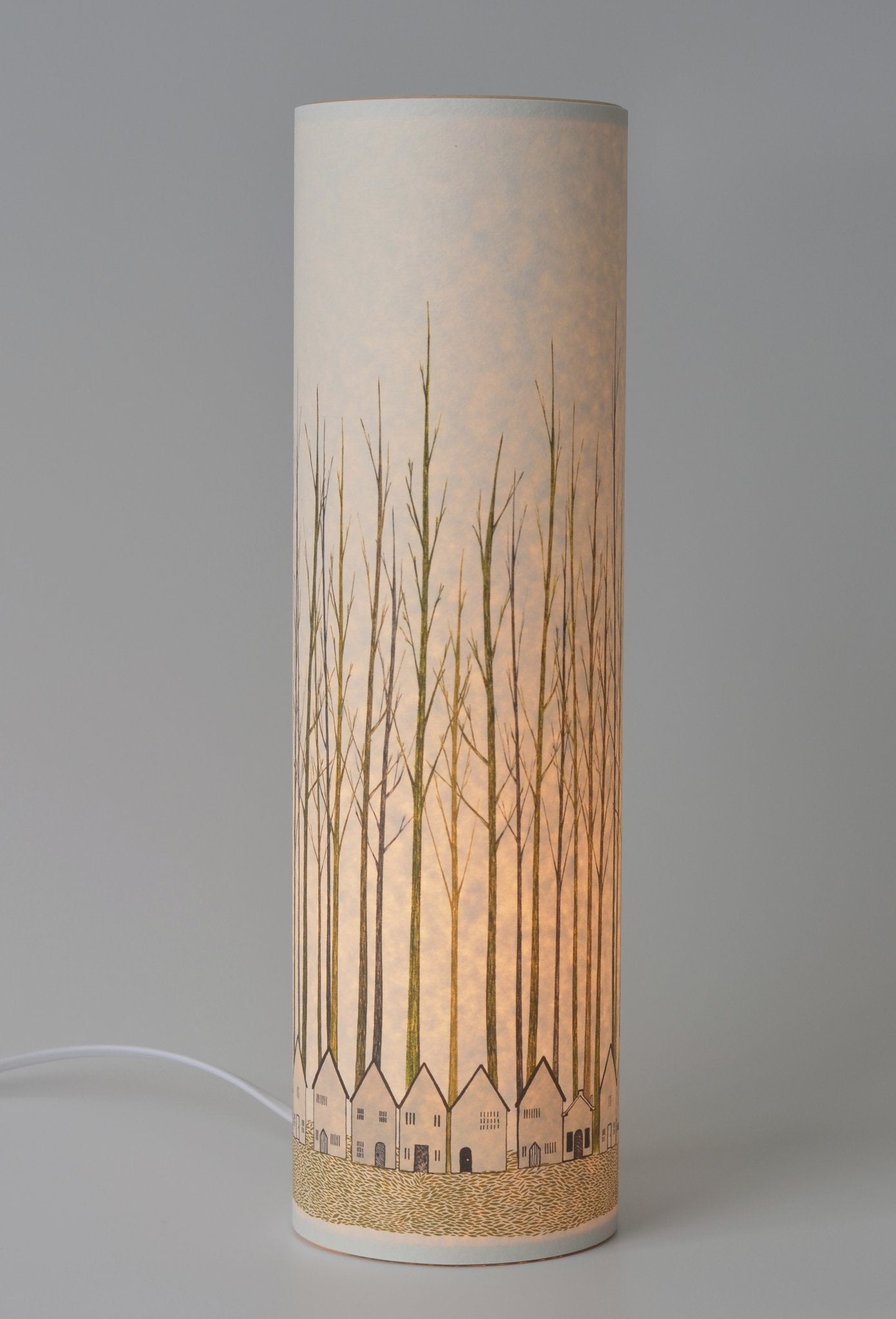 Cylindrical table lamp with a light-colored shade featuring an illustration of trees and houses.